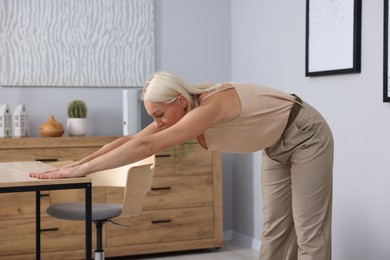 Photo of Mature woman stretching leaning on table in office