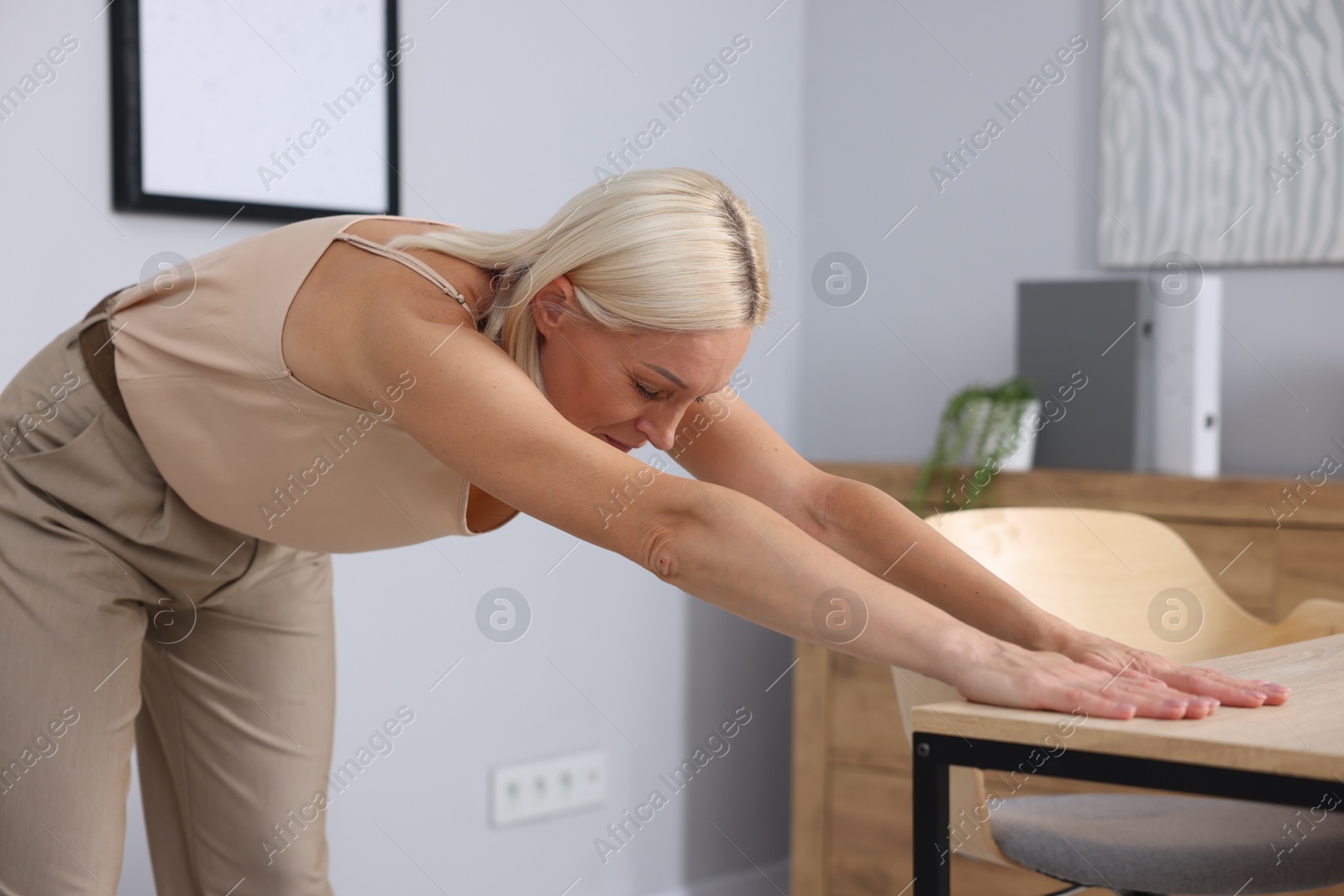 Photo of Mature woman stretching leaning on table in office