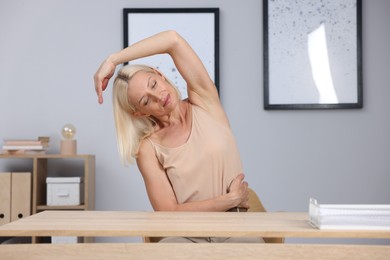 Photo of Mature woman stretching at table near grey wall