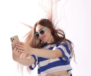 Photo of Happy woman in sunglasses with beautiful long hair using smartphone on white background