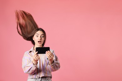 Photo of Surprised woman in jacket with beautiful long hair using smartphone on pink background. Space for text