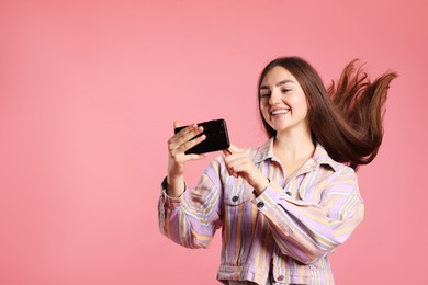 Photo of Happy woman in jacket with beautiful long hair using smartphone on pink background. Space for text