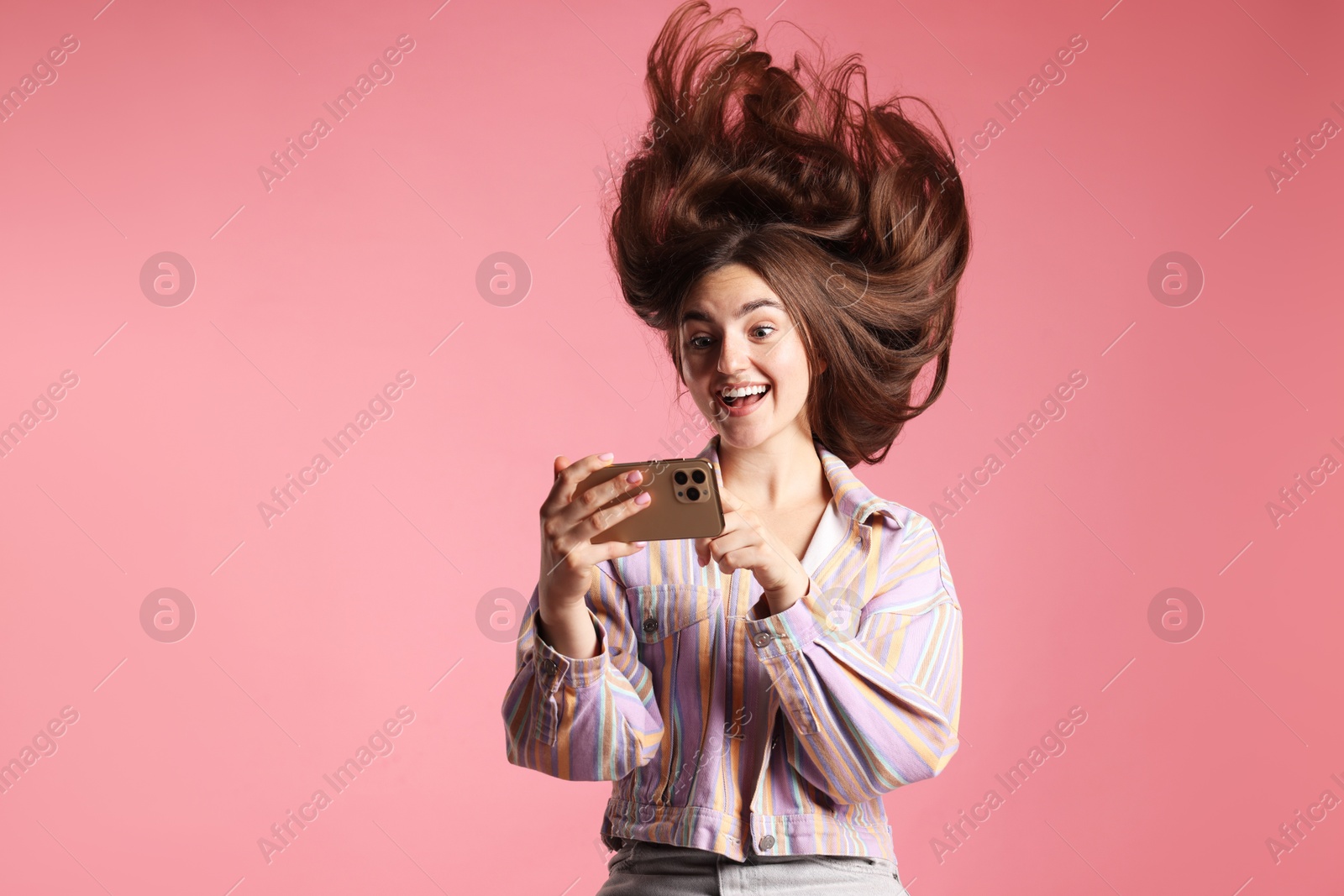 Photo of Happy woman in jacket with beautiful long hair using smartphone on pink background. Space for text
