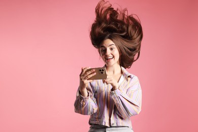 Photo of Happy woman in jacket with beautiful long hair using smartphone on pink background. Space for text