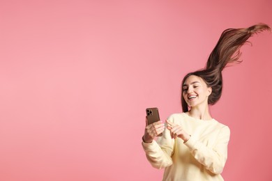 Photo of Happy woman with beautiful long hair using smartphone on pink background. Space for text