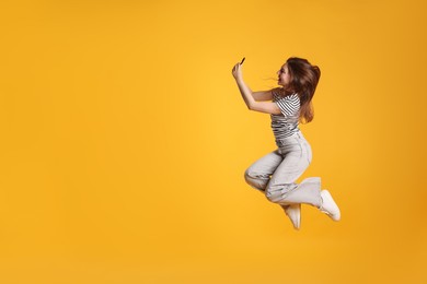 Photo of Happy woman with beautiful long hair using smartphone and jumping on orange background. Space for text