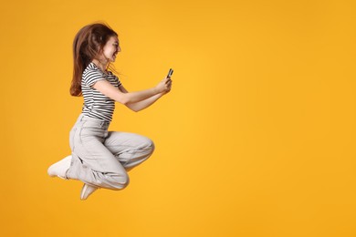 Photo of Happy woman with beautiful long hair using smartphone and jumping on orange background. Space for text