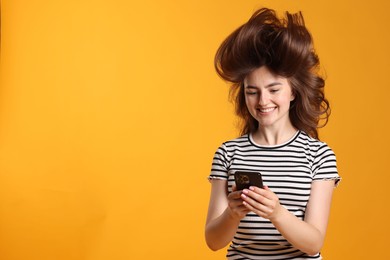 Photo of Happy woman with beautiful long hair using smartphone on orange background. Space for text