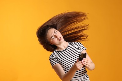 Photo of Emotional woman with beautiful long hair using smartphone on orange background. Space for text