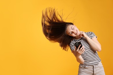 Photo of Happy woman with beautiful long hair using smartphone on orange background. Space for text