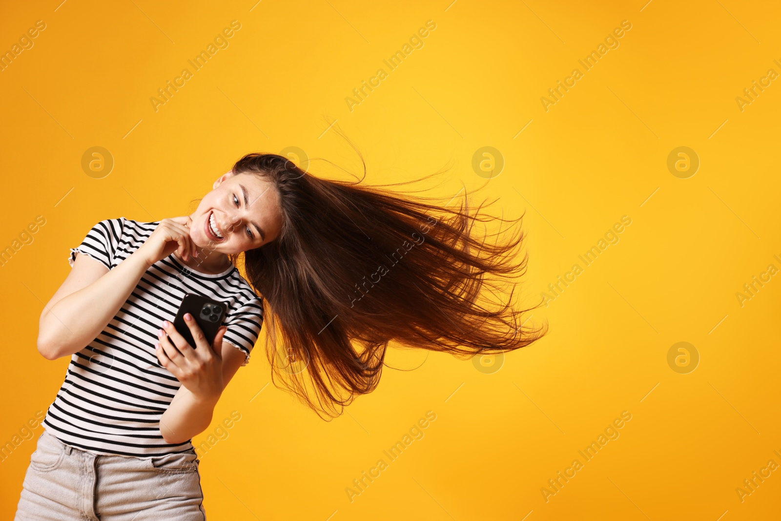 Photo of Happy woman with beautiful long hair using smartphone on orange background. Space for text