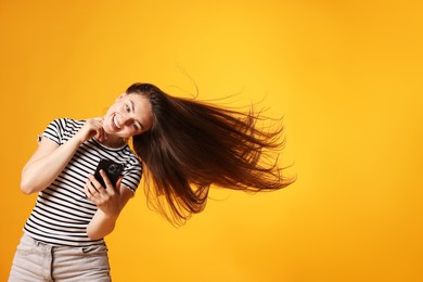 Photo of Happy woman with beautiful long hair using smartphone on orange background. Space for text