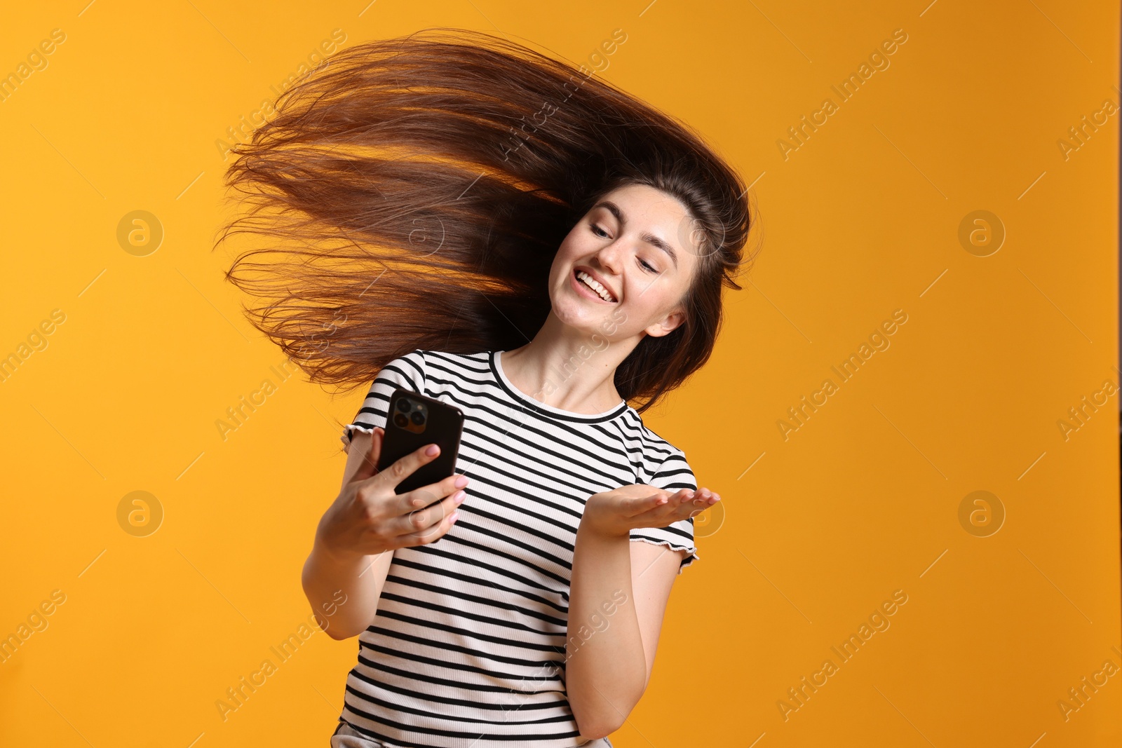 Photo of Happy woman with beautiful long hair using smartphone on orange background