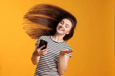 Photo of Happy woman with beautiful long hair using smartphone on orange background