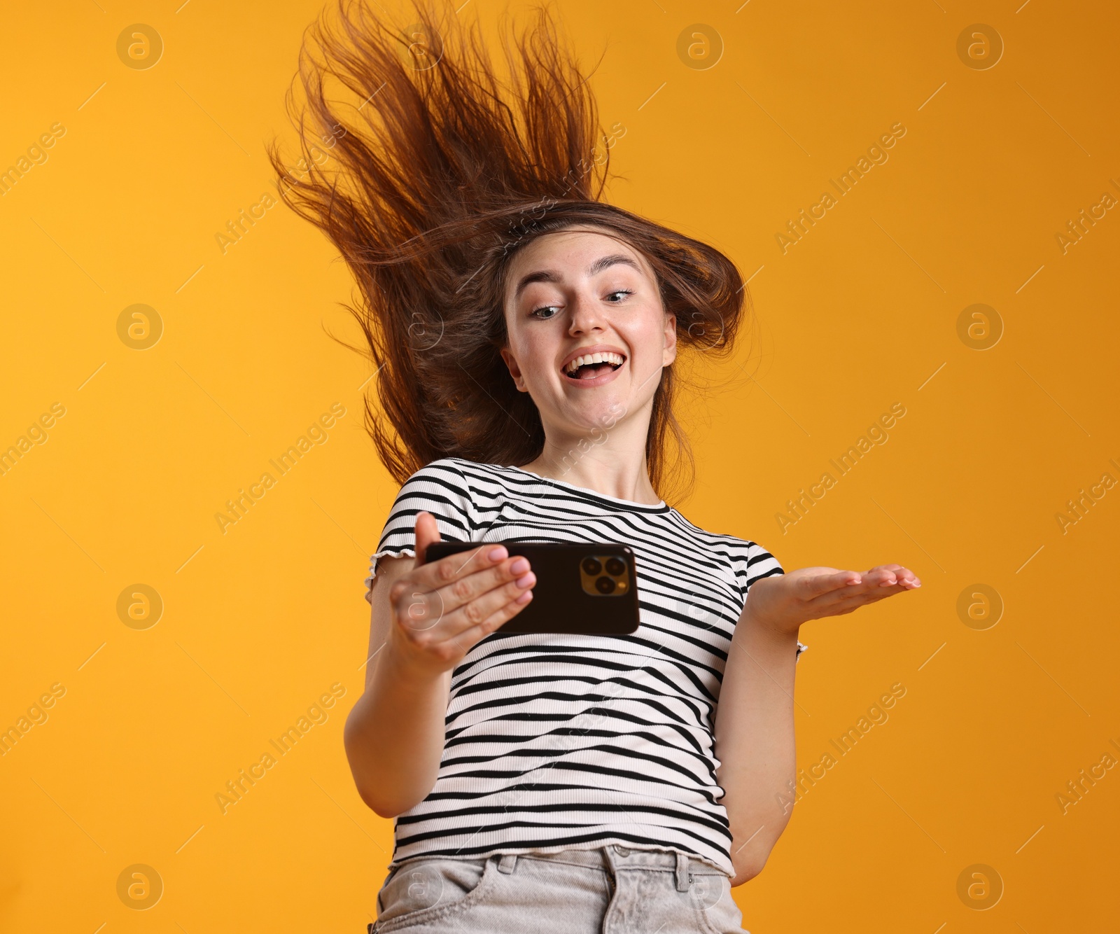 Photo of Happy woman with beautiful long hair using smartphone on orange background, low angle view