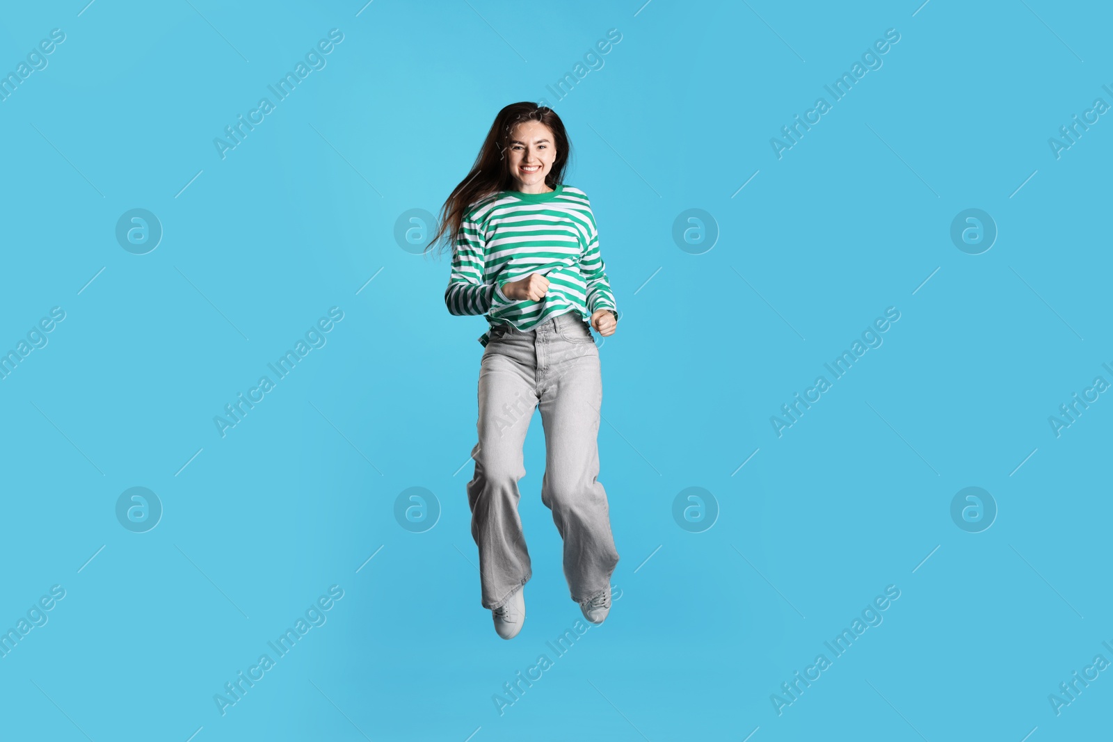 Photo of Happy woman with beautiful long hair jumping on light blue background