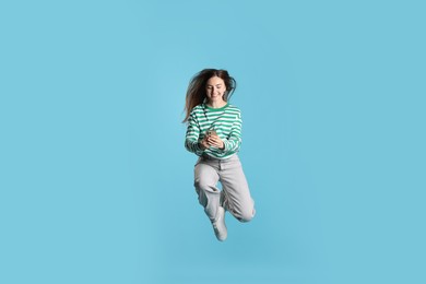 Photo of Happy woman with beautiful long hair using smartphone and jumping on light blue background