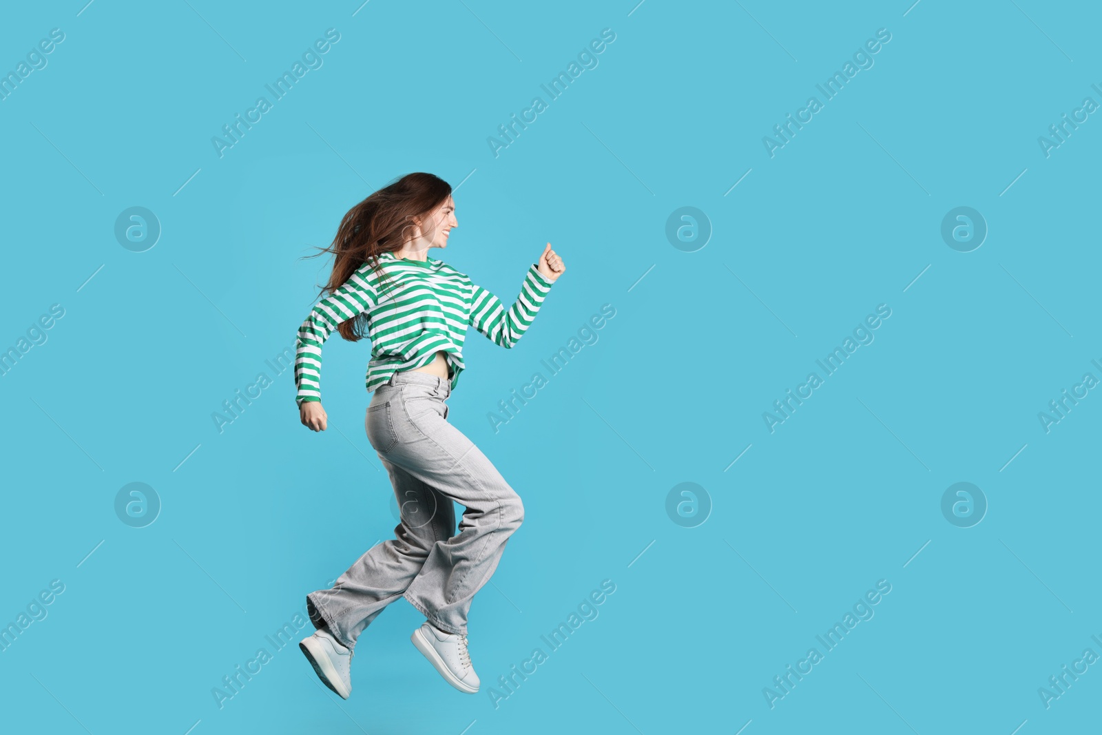 Photo of Happy woman with beautiful long hair jumping on light blue background. Space for text