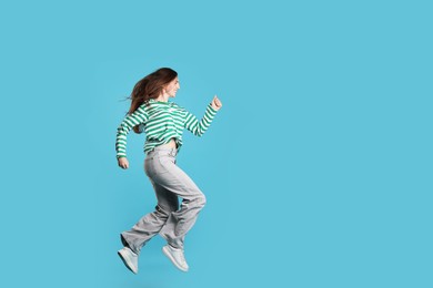 Photo of Happy woman with beautiful long hair jumping on light blue background. Space for text