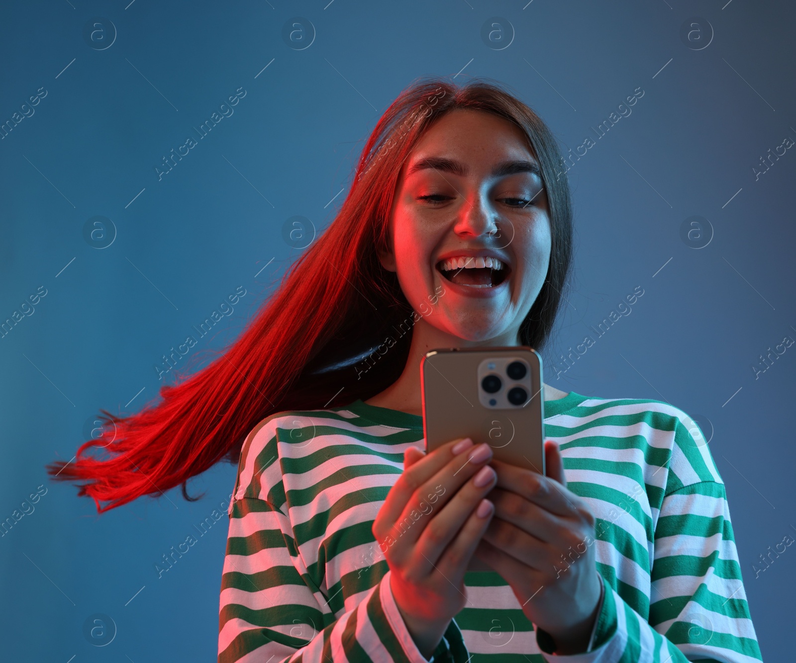 Photo of Happy woman with beautiful long hair using smartphone in neon lights against blue background