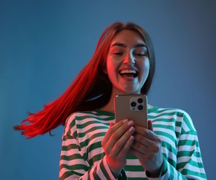 Photo of Happy woman with beautiful long hair using smartphone in neon lights against blue background