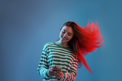 Photo of Happy woman with beautiful long hair using smartphone in neon lights against blue background