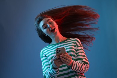 Photo of Emotional woman with beautiful long hair using smartphone in neon lights against blue background