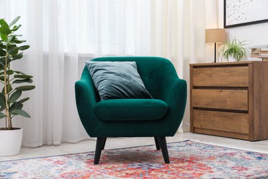 Photo of Stylish armchair with pillow, houseplant and chest of drawers indoors. Interior design