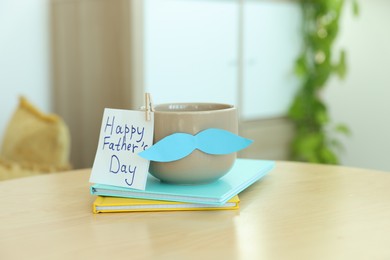 Photo of Happy Father's Day card, cup with mustache and notebooks on wooden table indoors