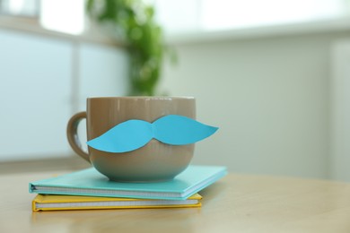 Photo of Happy Father's Day. Cup with mustache and notebooks on wooden table indoors, closeup. Space for text