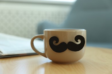 Photo of Happy Father's Day. Cup with mustache on wooden table indoors, closeup
