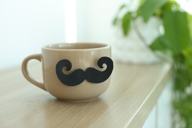 Photo of Happy Father's Day. Cup with mustache on wooden table indoors, closeup. Space for text