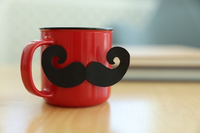Photo of Happy Father's Day. Cup with mustache and notebooks on wooden table indoors, closeup. Space for text