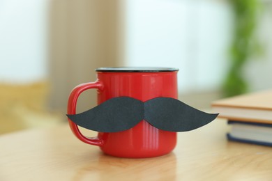 Photo of Happy Father's Day. Cup with mustache and notebooks on wooden table indoors, closeup