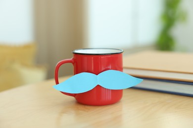 Photo of Happy Father's Day. Cup with mustache and notebooks on wooden table indoors