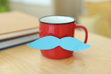 Photo of Happy Father's Day. Cup with mustache and notebooks on wooden table indoors, closeup