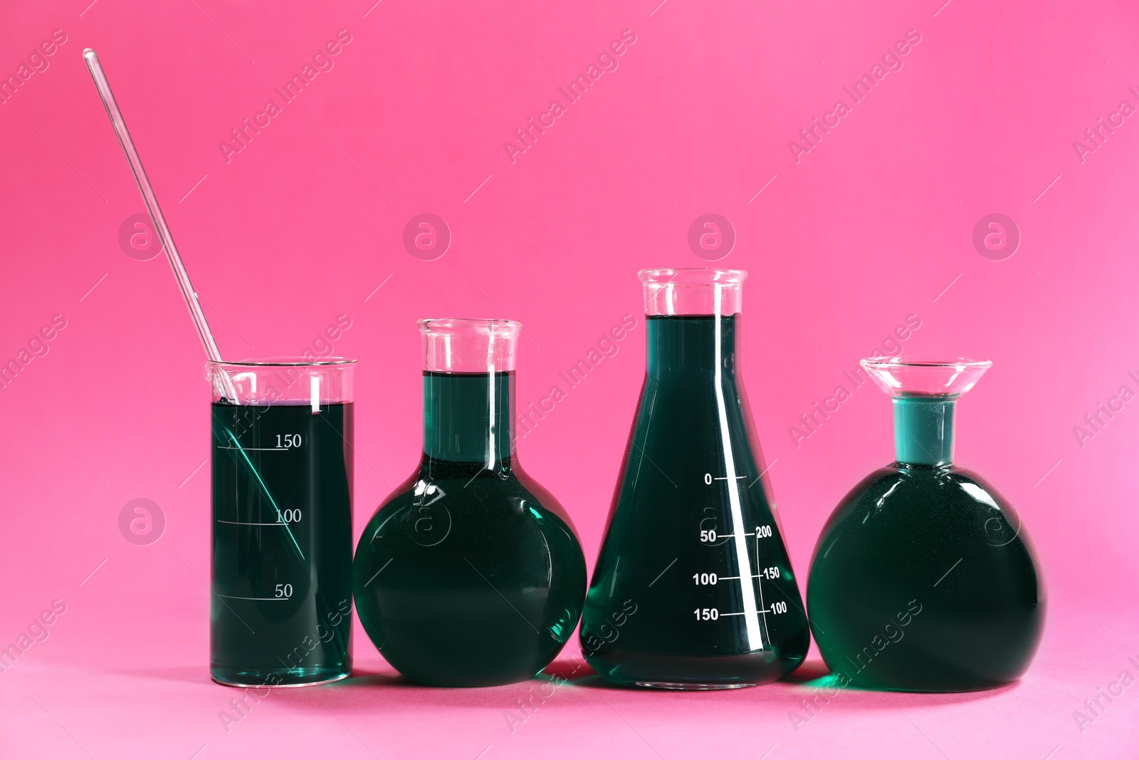 Photo of Laboratory glassware with green liquid on pink background