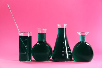 Photo of Laboratory glassware with green liquid on pink background
