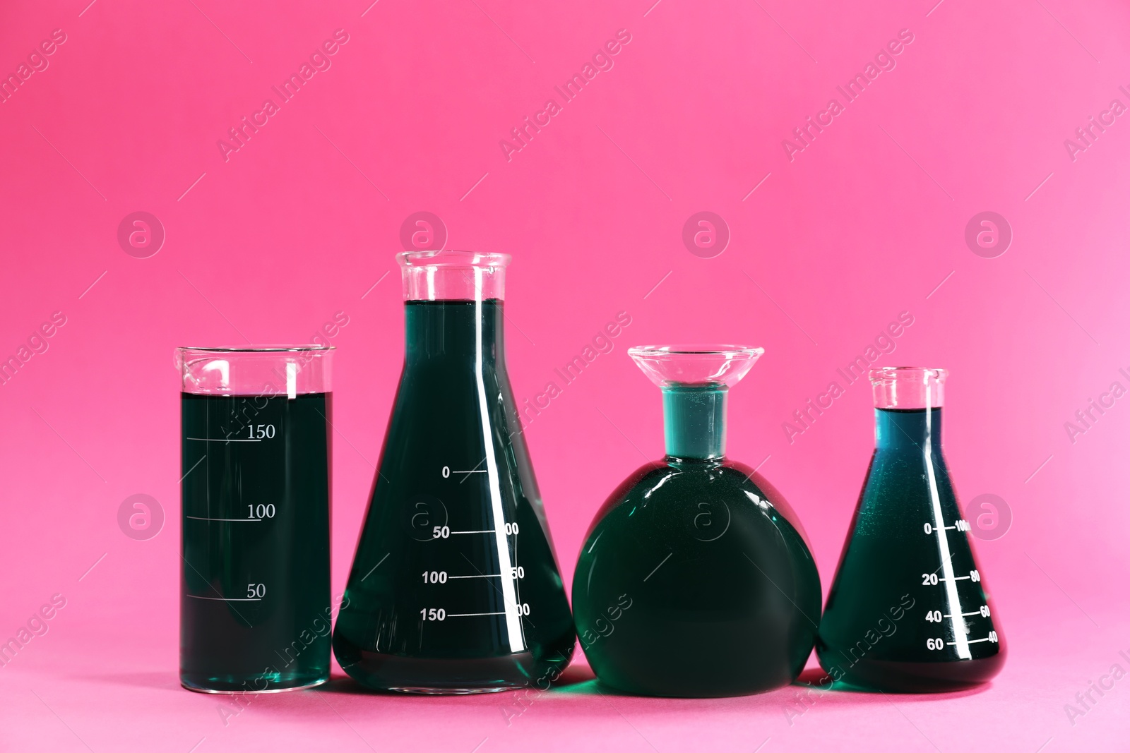 Photo of Laboratory glassware with green liquid on pink background. Space for text