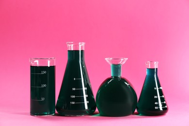 Photo of Laboratory glassware with green liquid on pink background. Space for text