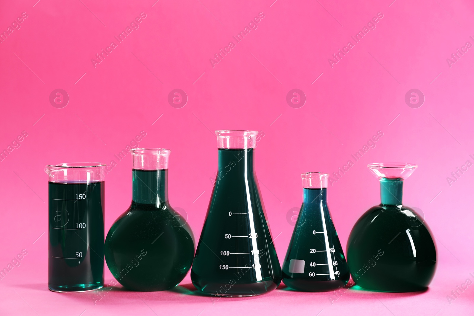 Laboratory glassware with green liquid on pink background. Space for text Photo of Laboratory glassware with green liquid on pink background. Space for text