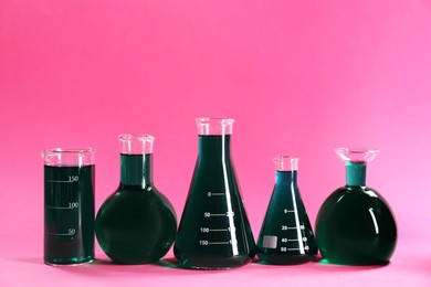 Photo of Laboratory glassware with green liquid on pink background. Space for text