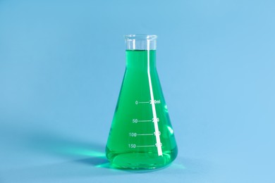 Photo of Conical flask with green liquid on light blue background
