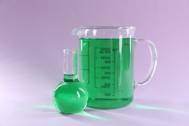 Photo of Laboratory glassware with green liquid on lilac background