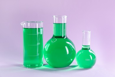 Photo of Laboratory glassware with green liquid on lilac background
