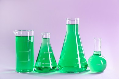 Photo of Laboratory glassware with green liquid on lilac background