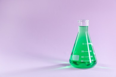 Photo of Conical flask with green liquid on lilac background. Space for text