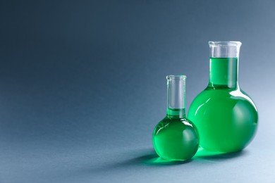 Photo of Laboratory glassware with green liquid on grey background. Space for text