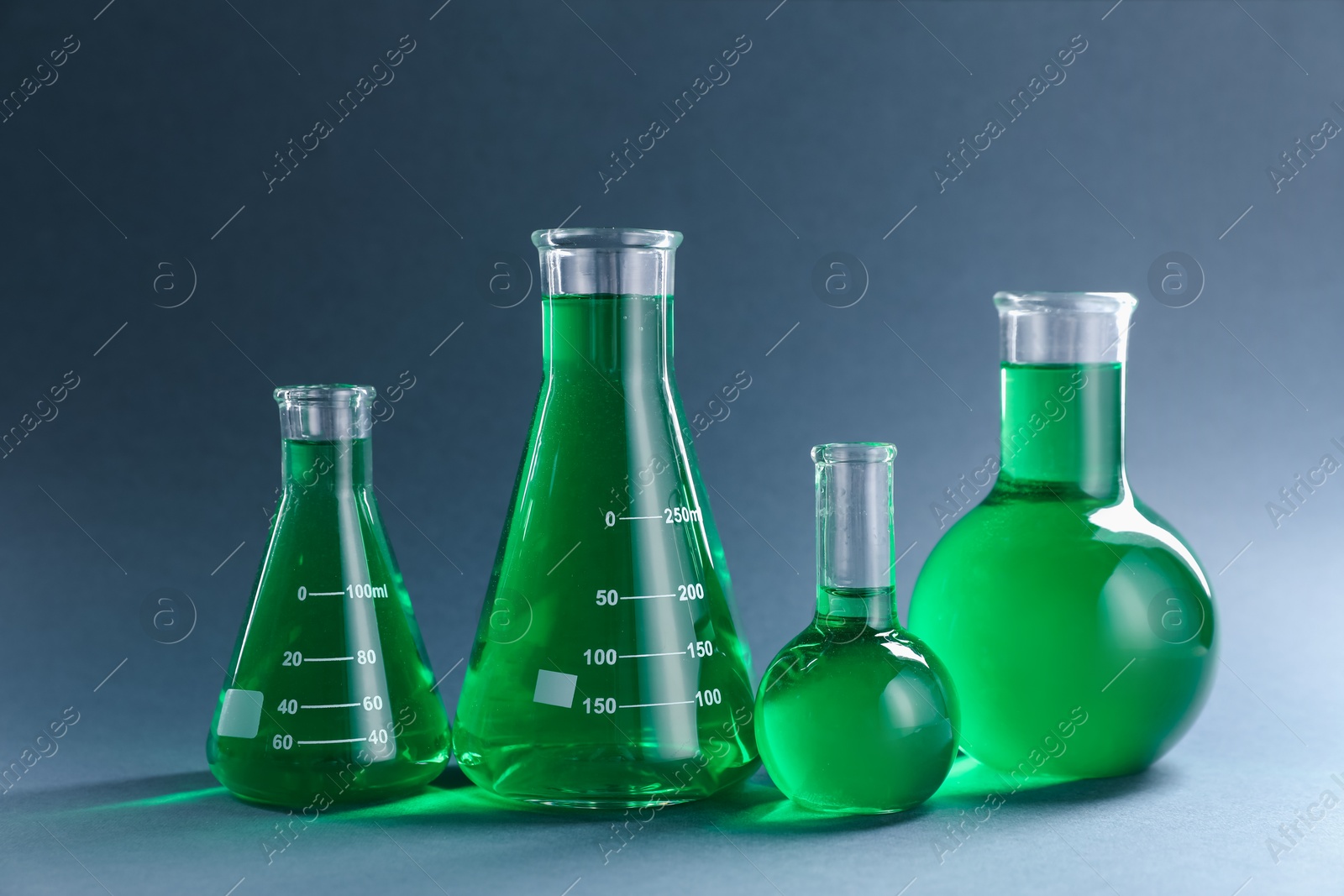 Laboratory glassware with green liquid on grey background Photo of Laboratory glassware with green liquid on grey background