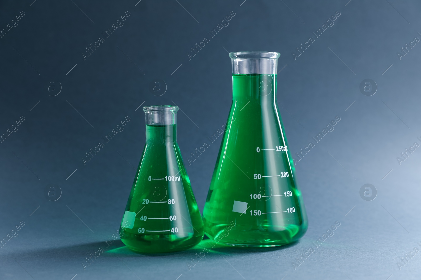 Laboratory glassware with green liquid on grey background Photo of Laboratory glassware with green liquid on grey background